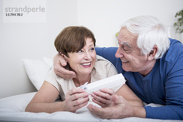 Seniorenpaar im Bett liegend  Mann verschenkt Frau