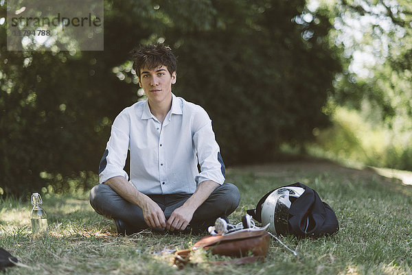 Porträt eines jungen Mannes  der auf einer Wiese im Park sitzt.