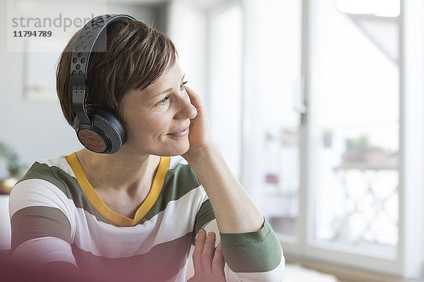 Lächelnde Frau hört Musik mit Kopfhörern zu Hause
