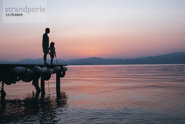 Italien  Lazise  Vater und kleine Tochter am Steg mit Blick auf den Gardasee bei Sonnenuntergang
