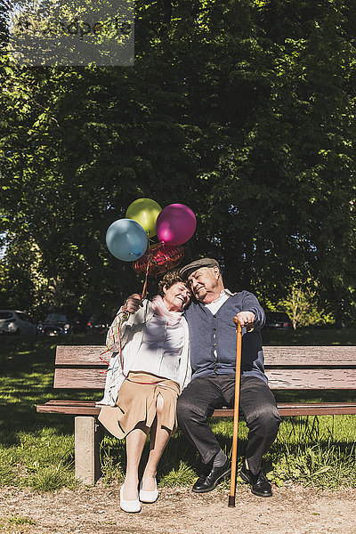 Glückliches Seniorenpaar mit Luftballons auf der Bank im Park