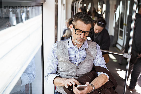 Geschäftsmann mit Smartphone und Kopfhörer  der in der Straßenbahn unterwegs ist.