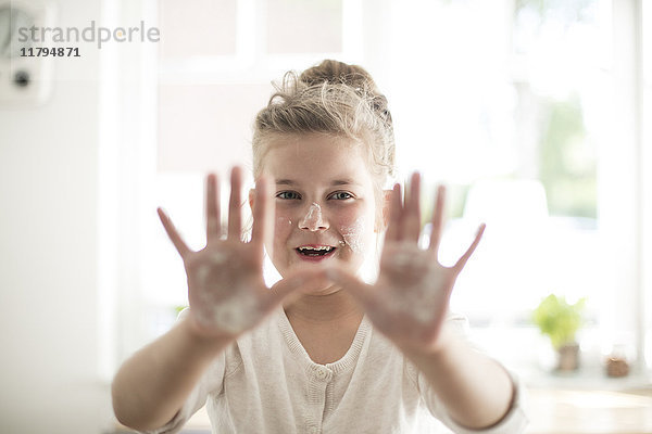 Porträt des lächelnden Mädchens in der Küche mit Teig auf Händen und Gesicht