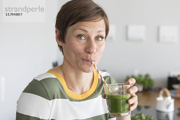 Porträt einer Frau  die in der Küche einen grünen Smoothie trinkt.
