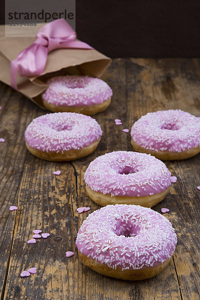 Doughnuts mit rosa Puderzucker und Zuckergranulat auf Holz