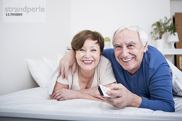 Seniorenpaar im Bett liegend mit Fernbedienung