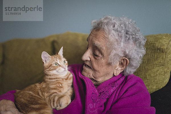 Seniorin sitzend mit Tabbykatze auf der Couch