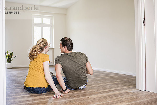 Junges Paar in neuem Zuhause sitzt auf dem Boden und diskutiert