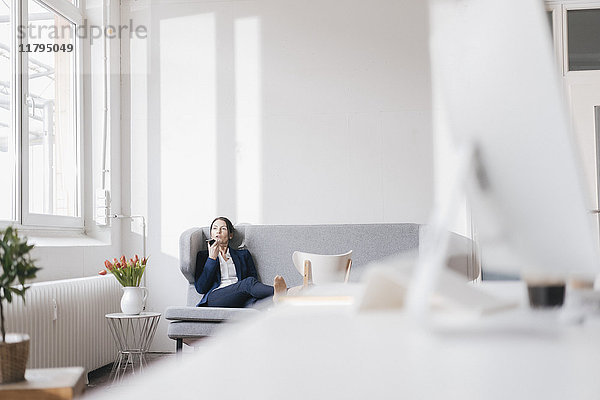 Geschäftsfrau sitzt auf der Couch in einem Loft mit Handy