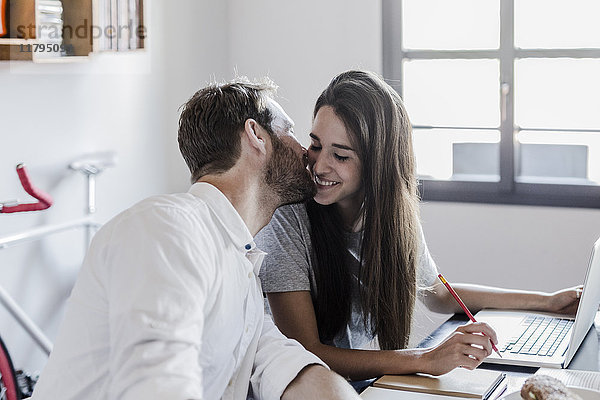 Glückliches Paar mit Laptop zu Hause küssen