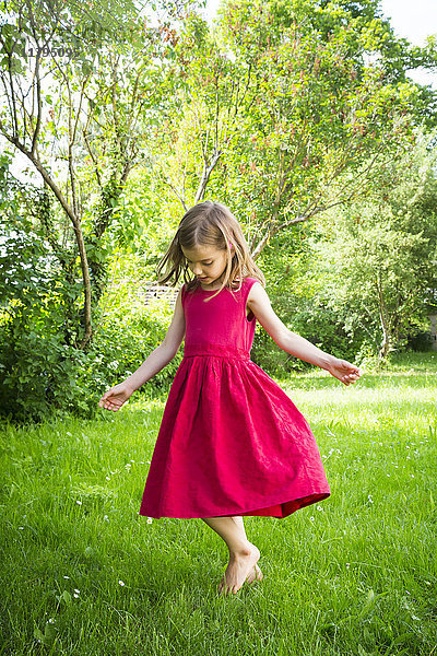 Kleines Mädchen in rotem Sommerkleid tanzt auf einer Wiese