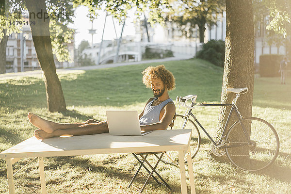 Mann mit Bart und lockigem Haar mit Laptop am Tisch im Park