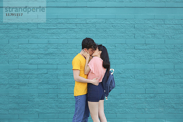 Junges Paar küsst sich vor blauer Ziegelwand