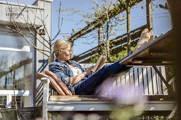 Lächelnde Frau liest Buch auf Gartenbank