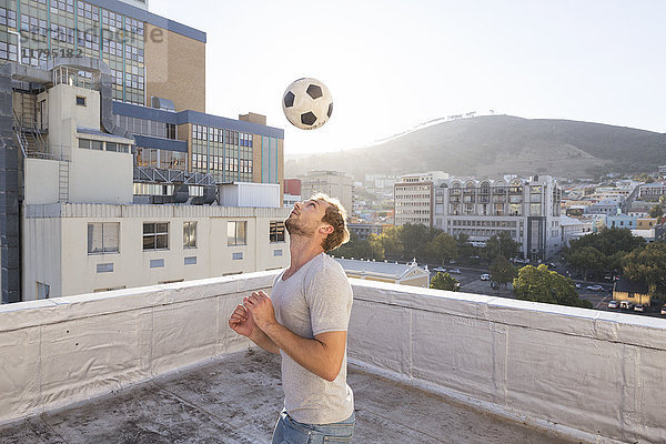 Junger Mann spielt Fußball auf der Dachterrasse