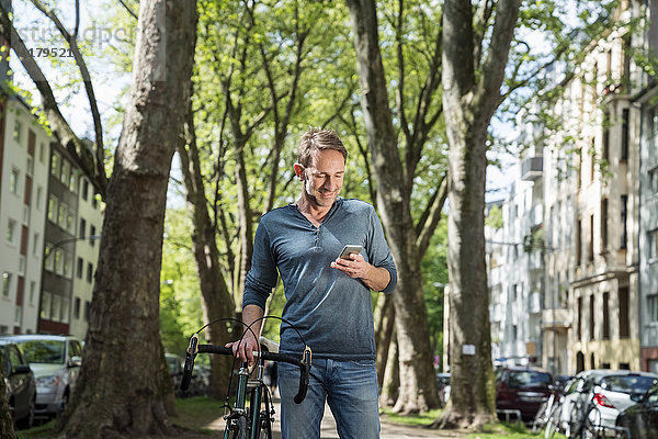 Lächelnder reifer Mann mit Fahrrad in der Stadt beim Blick aufs Handy