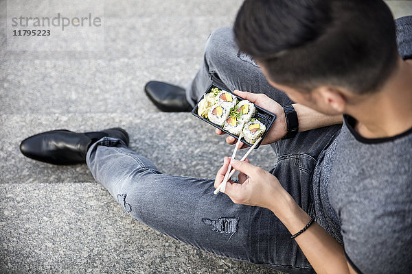 Mann sitzt auf der Treppe und isst Sushi zum Mitnehmen.