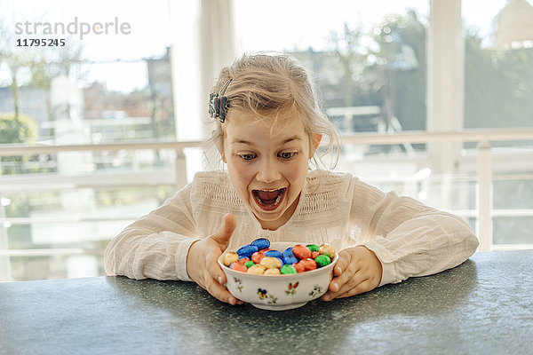Aufgeregtes Mädchen mit Schokoladen-Ostereiern auf dem Tisch