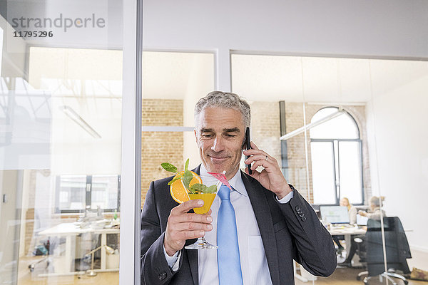 Ein reifer Geschäftsmann trinkt einen Cocktail  während er telefoniert.