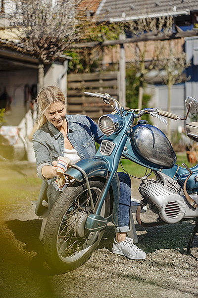 Lächelnde Frau reinigt Oldtimer-Motorrad