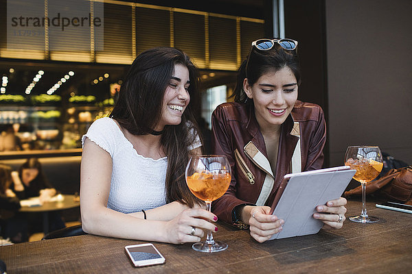 Zwei glückliche junge Frauen  die in einer Bar auf die Tafel schauen.