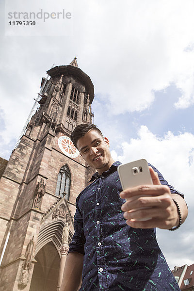 Deutschland  Freiburg  junger Mann  der einen Selfie an der Klosterkirche nimmt