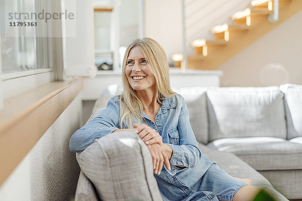 Lächelnde Frau zu Hause auf der Couch sitzend