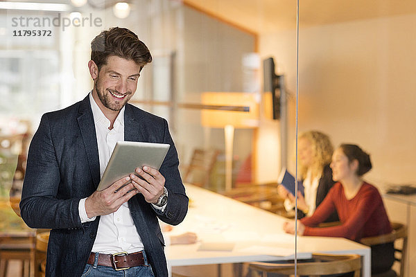 Jungunternehmer im Büro mit digitalem Tablett  mit Mitarbeitern im Hintergrund