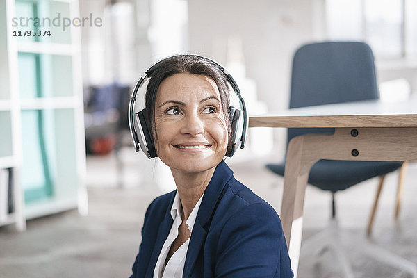 Porträt einer lächelnden Geschäftsfrau in einem Loft  die mit Kopfhörern Musik hört.