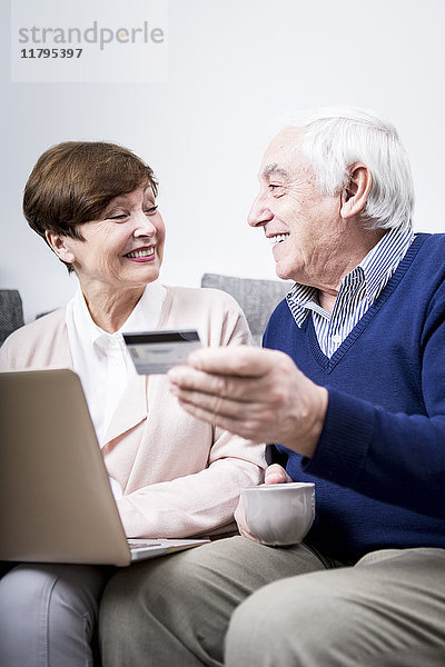 Seniorenpaar auf der Couch liegend beim Online-Shopping mit Kreditkarte