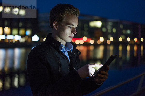 Junger Mann mit Tablette im Freien bei Nacht
