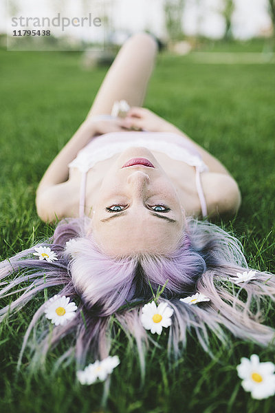 Porträt einer auf Gras liegenden Frau mit Blumen auf Haaren