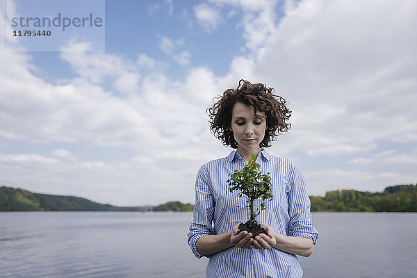 Frau am See hält kleinen Baum in der Hand
