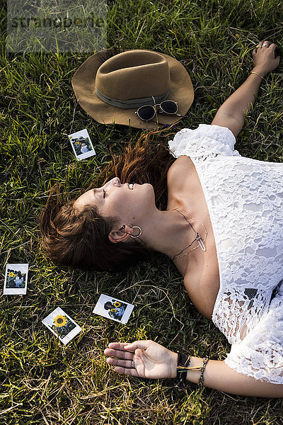 Glückliche Frau liegt auf einem Feld  umgeben von Sofortbildern.