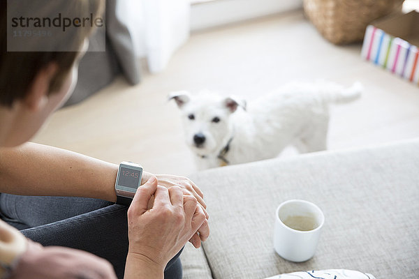 Frau sitzt zu Hause auf der Couch und schaut auf smartwatch