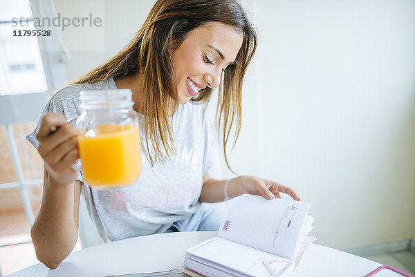 Lächelnde junge Frau mit einem Glas Orangensaft auf der Agenda