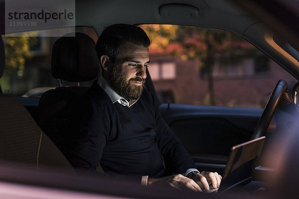Geschäftsmann mit Laptop im Auto bei Nacht