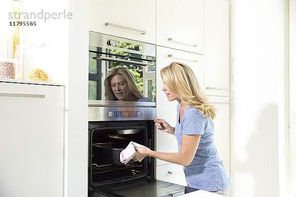 Frau in der Küche nimmt Auflaufform aus dem Ofen