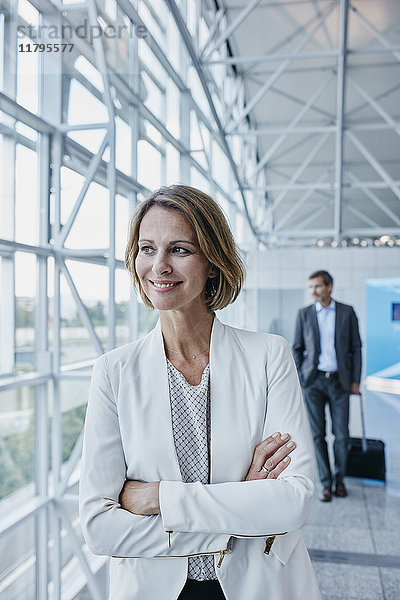 Lächelnde Geschäftsfrau am Flughafen mit Blick aus dem Fenster
