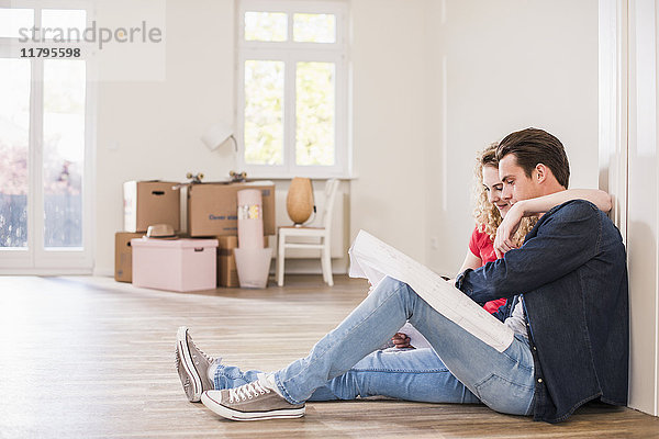 Junges Paar in neuem Zuhause auf dem Boden sitzend mit Blick auf den Grundriss