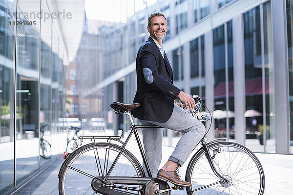 Lächelnder Geschäftsmann auf dem Fahrrad in der Stadt