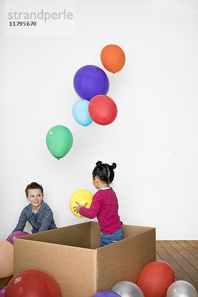 Zwei Kinder spielen mit Ballon und Pappschachtel