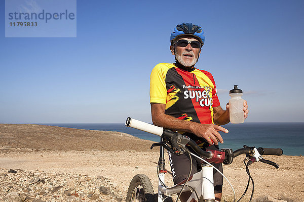 Spanien  Kanarische Inseln  Fuerteventura  älterer Mann mit Mountainbike beim Ausruhen