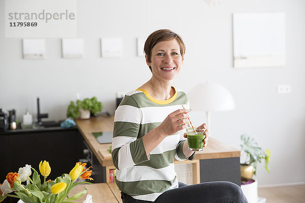 Porträt einer lächelnden Frau mit grünem Smoothie in der Küche
