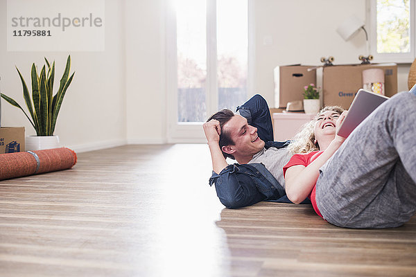 Glückliches junges Paar in neuem Zuhause auf dem Boden liegend mit Tablette