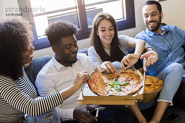 Glückliche Freunde sitzen auf dem Sofa und teilen sich eine Pizza.