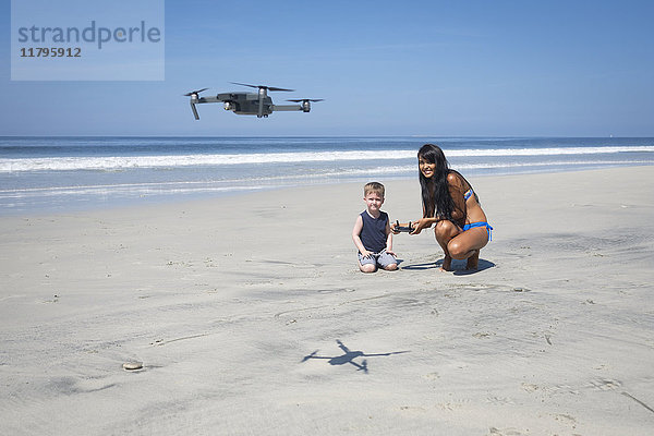Junge Frau und Junge am Strand fliegende Drohne