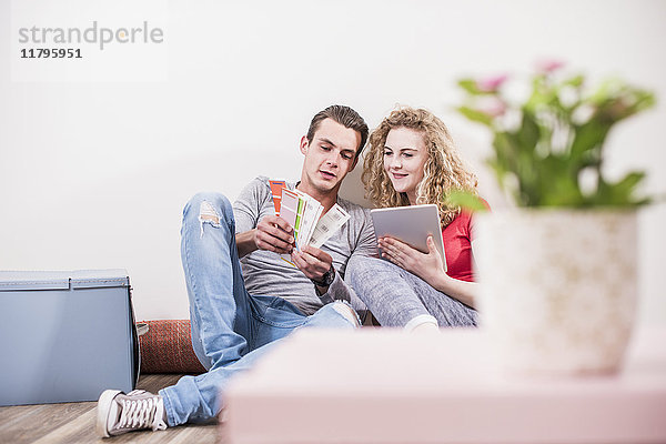 Junges Paar in neuem Zuhause auf dem Boden sitzend mit Tablette aus Farbmuster auswählen