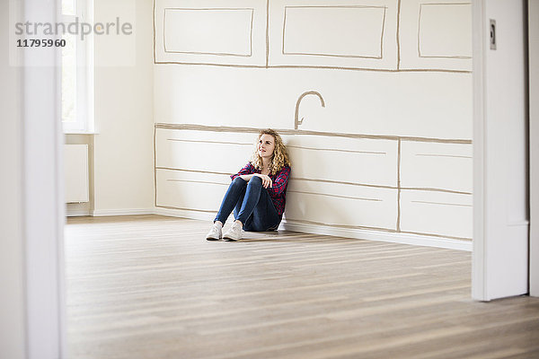 Junge Frau im neuen Zuhause sitzt auf dem Boden und denkt über Innenarchitektur nach.