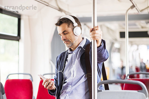 Geschäftsmann mit Smartphone und Kopfhörer auf Busfahrt
